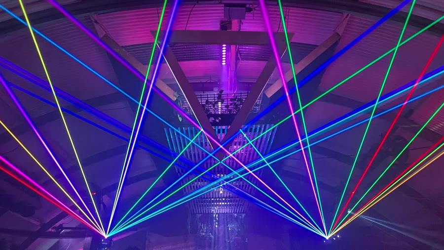 Two laser projectors casting fans of multi-coloured beams across a small venue, by Dam Lasers