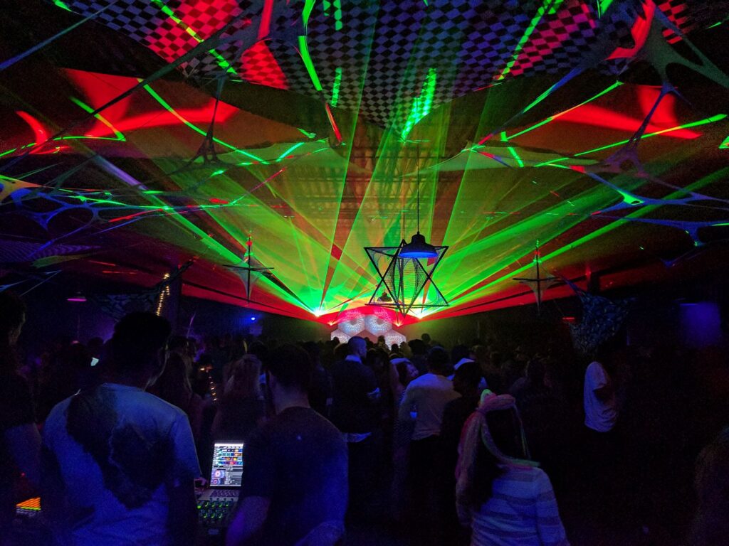 Green laser canopy spread over a large warehouse crowd, with a hanging geometric star structure