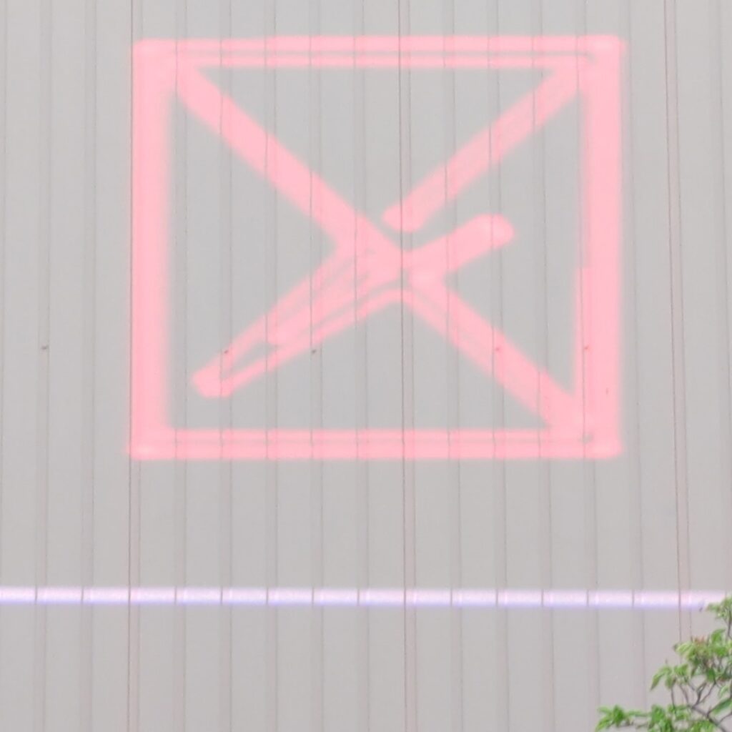 Red laser logo, a square crossed by a diagonal, projected onto a white corrugated metal wall