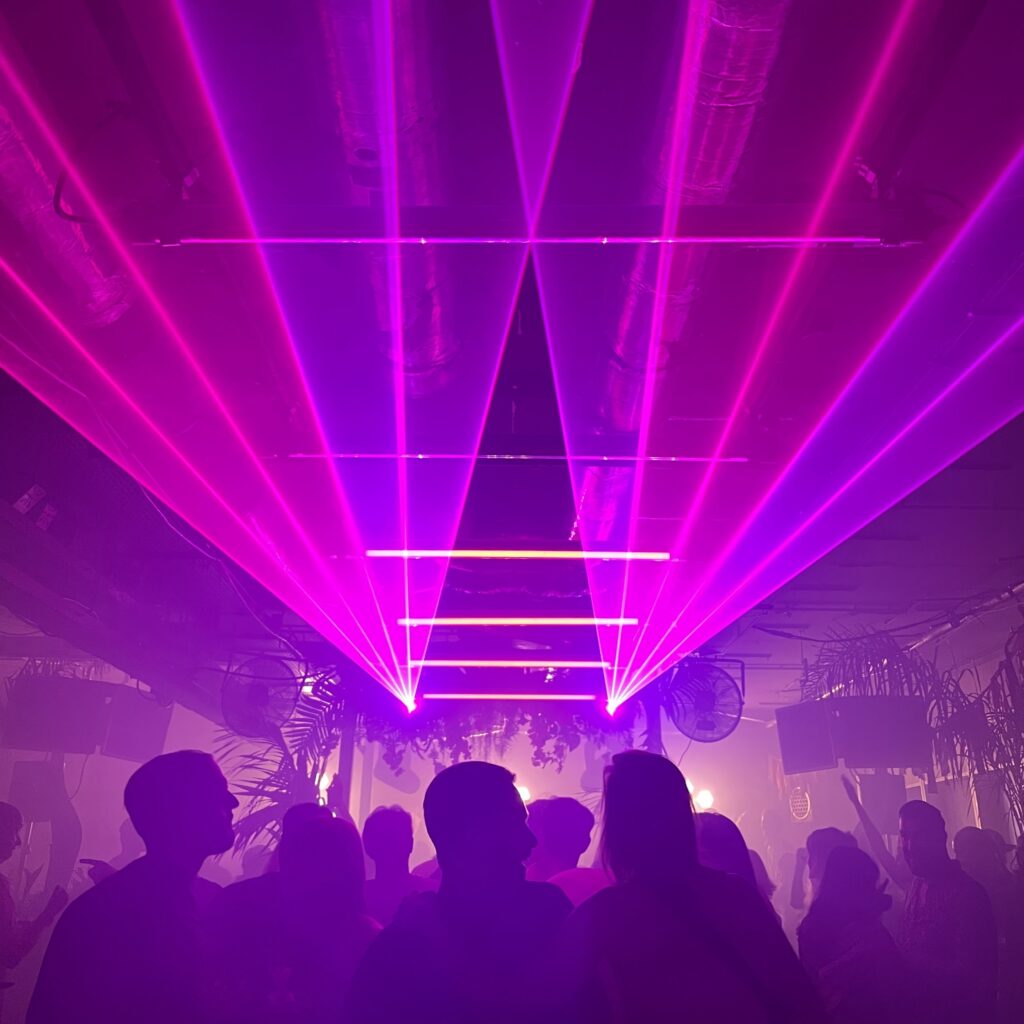Magenta laser beams fanning across the ceiling of a small club above a crowd of silhouetted dancers