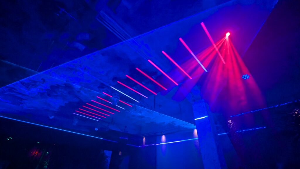 Red laser beams fanning down through a blue-lit club interior with a low concrete ceiling