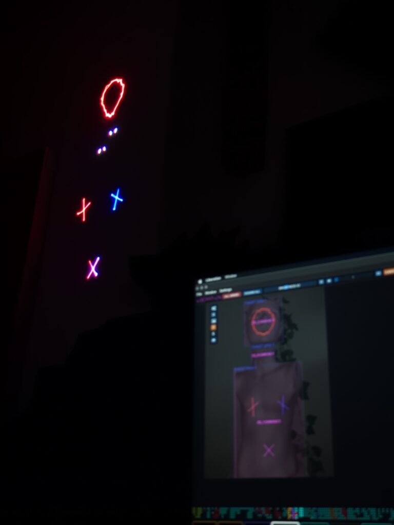 Small red and blue laser shapes projected in a dark room beside a laptop running mapping software