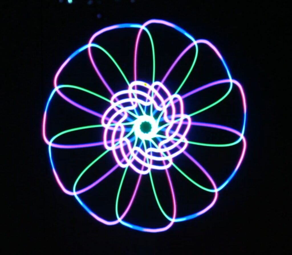 Symmetrical laser graphic like a multi-petalled flower, drawn in cyan, magenta and green